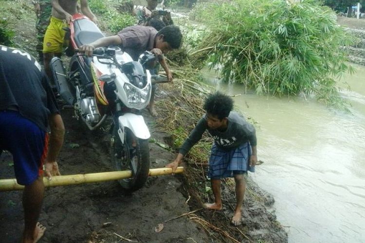 Kendaraan motor warga saat hendak dipikul melewati sungai karena salahsatu jembatan yang merupakan akses alternatif di Kecamatan Soromandi, Kabupaten Bima, ambruk diterjang banjir pada Kamis (15/02/2018)