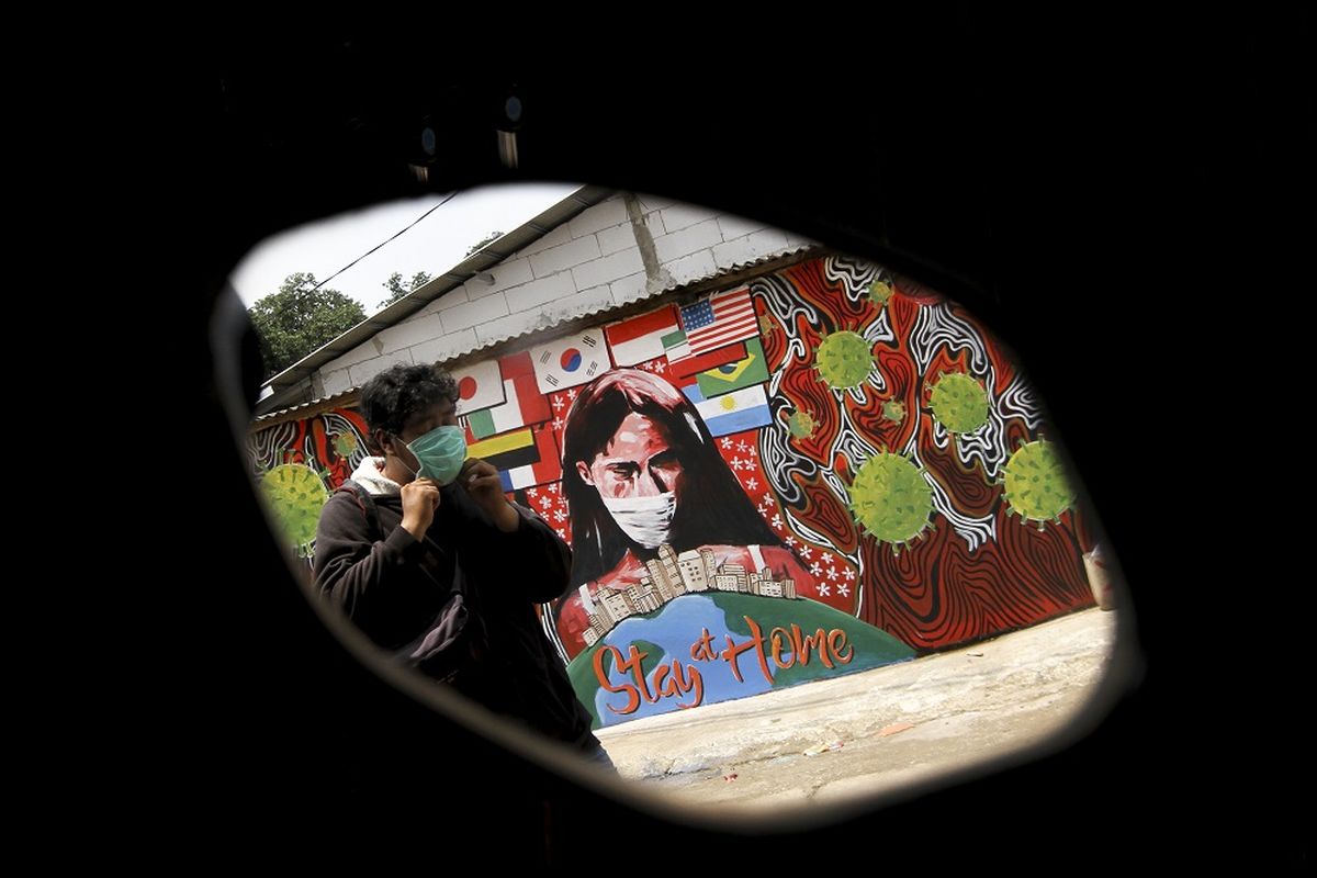 Seorang Warga melintas di depan mural bertuliskan Stay At Home di Cipayung, Depok, Jawa Barat, Selasa (14/4/2020). Pemerintah Kota Depok akan menerapkan Pembatasan Sosial Berskala Besar (PSBB) mulai Rabu (15/4) sebagai upaya memutus rantai penyebaran virus corona COVID-19. ANTARA FOTO/Asprilla Dwi Adha/hp.