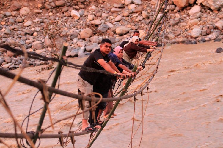 Sejumlah warga melintasi jembatan alternatif yang menghubungkan Desa Blang Meurandeh dan Desa Blang Puuk Beutong Ateuh Banggalang, Nagan Raya, Aceh, Minggu (30/11/2025). Pasca putusnya jembatan gantung diterjang banjir bandang pada Rabu (26/11) warga membuat jembatan darurat dari tali jembatan tersebut untuk jalur alternatif.