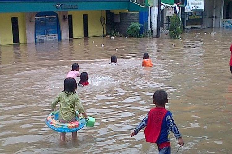 Anak-anak bermain di genangan air depan selter transJakarta Bidara Cina, Jakarta Timur, Minggu (19/1/2014).