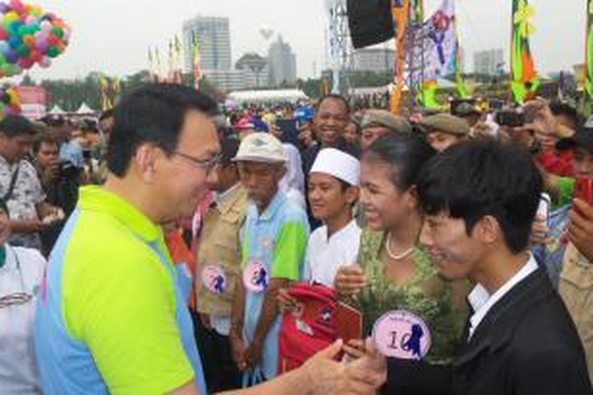 Gubernur DKI Jakarta Basuki Tjahaja Purnama menyerahkan buku nikah kepada salah satu pengantin dalam acara peringatan Hari Kesetiakawana  Sosial Nasional di Lapangan Monas, Sabtu (13/12/2014)