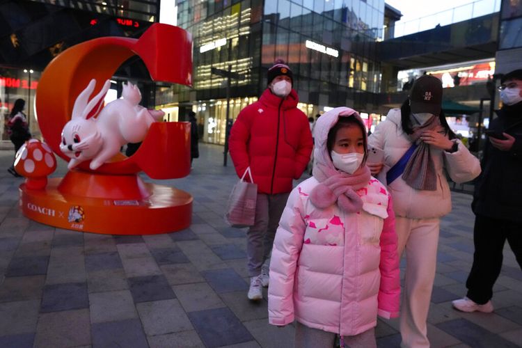 Warga memakai masker melewati iklan merek bergambar kelinci menjelang Tahun Baru Imlek mendatang di Beijing, Minggu (1/1/2023).