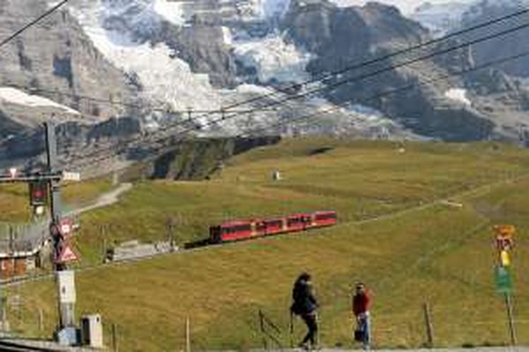 Wisatawan berpose dengan latar belakang kereta api listrik bergerigi (cogwheel) rute Jungfraujoch-Kleine Scheidegg yang tengah melaju di dinding Pegunungan Alpen, Swiss, pertengahan September lalu. Kereta api yang dikelola Jungfrau Railway ini merupakan satu-satunya transportasi menuju tempat wisata Jungfraujoch yang disebut juga top of Europe.
