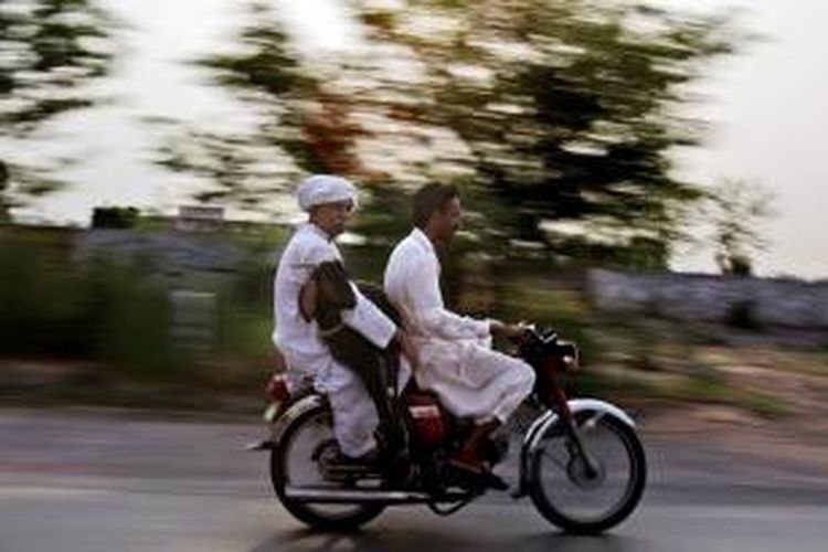 Dalam foto yang diambil pada Juni 2011 ini terlihat dua warga Pakistan tengah berboncengan menunggang sepeda motor sambil membawa kambing di pinggiran kota Lahore.