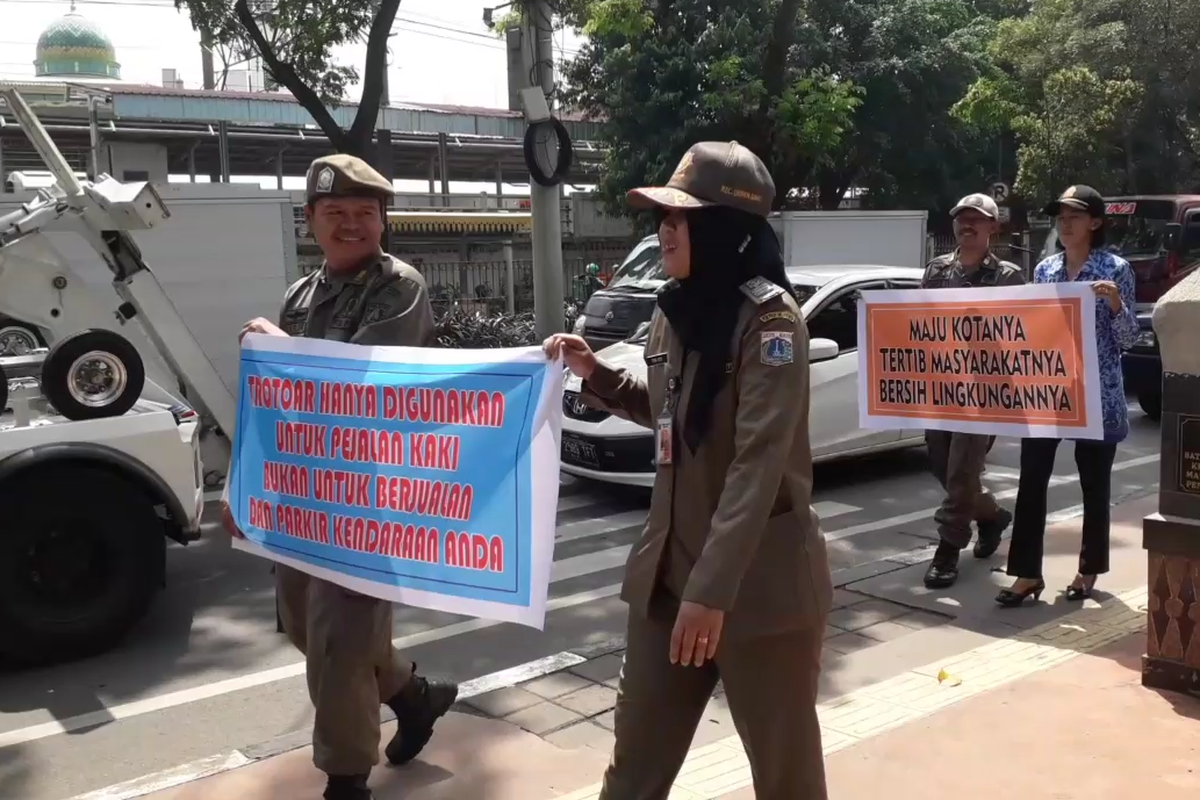 Petugas Satuan Polisi Pamong Praja Duren Sawit menyosialisasikan larangan berdagang dan parkir di atas trotoar di Jalan I Gusti Ngurah Rai, Kamis (25/4/2019).