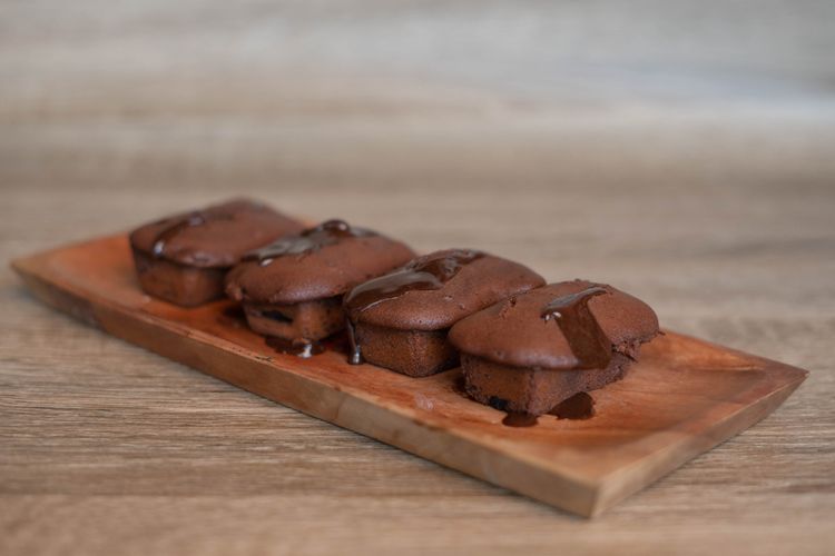 Ilustrasi kue balok cokelat di atas piring saji kayu. 
