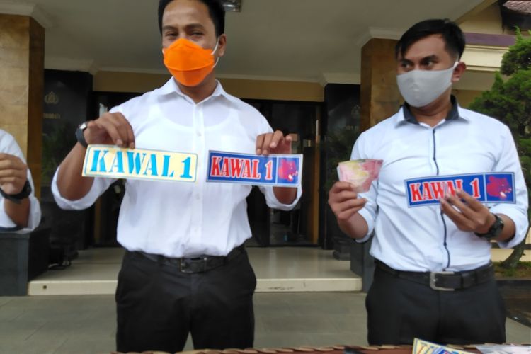 Petugas kepolisian tengah memperlihatkan stiker bebas PSBB provinsi Jabar yang dijual secara paksa oleh kelima tersangka untuk memuluskan pungutan liar yang dilakukan mereka.