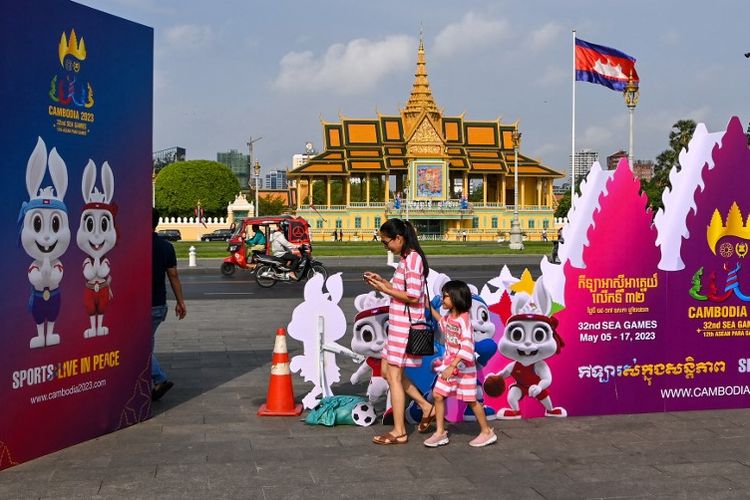 Seorang wanita dan anaknya berjalan di dekat papan yang menunjukkan maskot SEA Games 2023 menjelang opening ceremony atau upacara pembukaan di Stadion Modorok Techno, Phnom Penh, Kamboja, Kamis (4/5/2023). Artikel ini berisi jadwal siaran langsung opening ceremony SEA Games 2023 Kamboja. (Photo by TANG CHHIN Sothy / AFP)