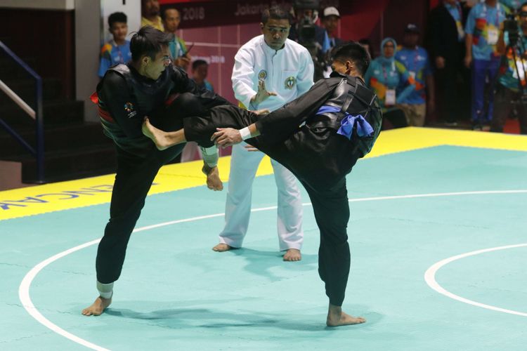 Pesilat Indonesia Komang Harik Adi Putra (sabuk merah) melakukan serangan  kepada pesilat Malaysia Mohd Al Jufferi Jamari dalam babak final Kelas E Putra Asian Games 2018 di Padepokan Pencak Silat Taman Mini Indonesia Indah (TMII), Jakarta, Senin (27/8/2018). Komang berhasil meraih medali emas cabang olahraga pencak silat kelas 65-70 kilogram.