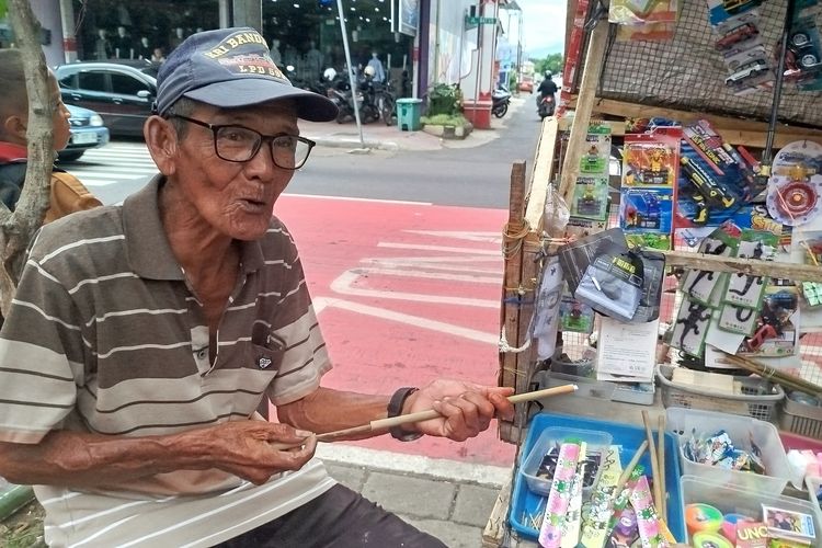 Ahmad mempraktekkan mainan tradisional tembak bambu yang dijualnya di depan SDN Lateng Banyuwangi, Sabtu (11/1/2025). 