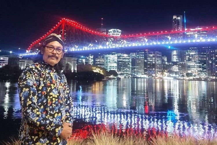 Agustinus Jogiono, warga asal Yogyakarta yang tinggal di Brisbane, Australia, mengenakan blangkon dan surjan ketika berpose di depan jembatan Brisbane yang berwarna merah putih pada Senin (17/8/2020). Cahaya merah putih tersebut merupakan bentuk ikut merayakan 75 tahun kemerdekaan Indonesia.