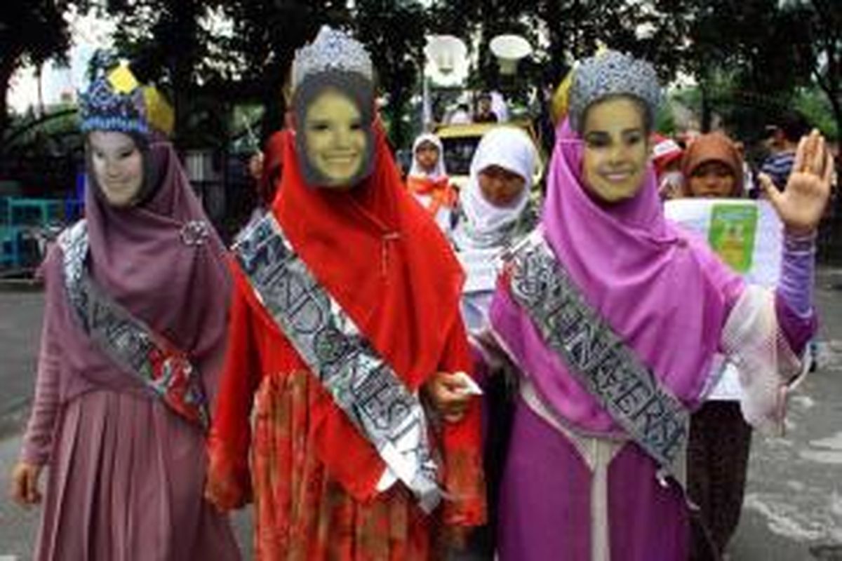 Anggota Hizbut Tahrir Indonesia mengenakan topeng dan selendang ala Miss World, Miss Universe and Miss Indonesia saat berunjuk rasa di Medan, 5 September 2013, menentang penyelenggaraan kontes Miss World.
