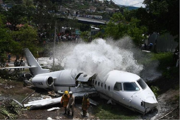 Pasukan pemadam kebakaran menyemprotkan busa ke tubuh pesawat yang terbelah setelah tergelincir di bandara Toncontin, Honduras untuk mencegah munculknya api.