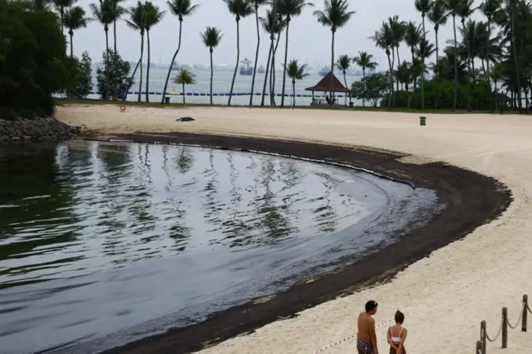 Para pengunjung berjalan di bibir pantai yang dilapisi minyak di Pantai Tanjong pada Minggu.