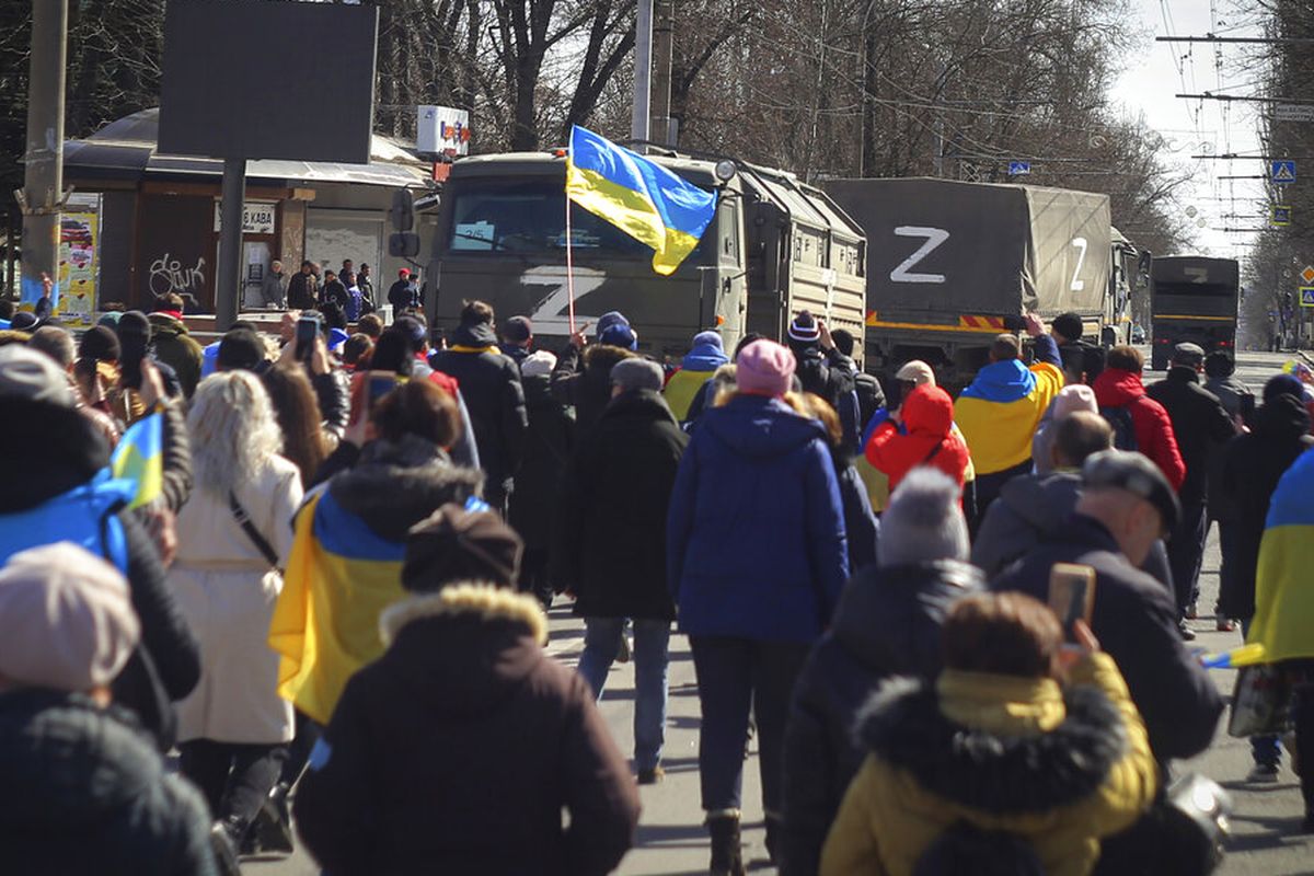 Orang-orang membawa bendera Ukraina berjalan menuju truk tentara Rusia saat unjuk rasa menentang pendudukan Rusia di Kherson, Ukraina, Minggu (20/3/2022). PBB mengecam intimidasi yang dilakukan Rusia terhadap warga yang menentang perang Rusia. Sementara pada Selasa (28/9/2022), hasil referendum di empat wilayah Ukraina, termasuk di Kherson mengarah pada bergabung dengan Rusia. Rusia bisa kehilangan 15 persen wilayahnya.