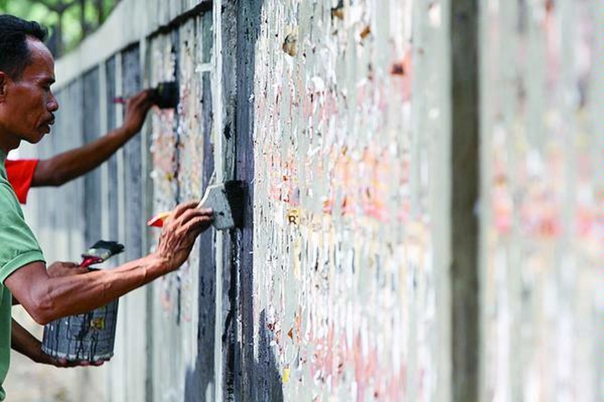 Pegawai Kelurahan Benhil mengerik poster atribut kampanye dan menutupnya dengan cat hitam di Jalan Karet Pasar Baru Barat, Tanah Abang,  Jakarta, Senin (9/7). Mereka menyayangkan tim sukses pasangan calon gubernur dan wakil gubernur yang tidak total membersihkan atribut kampanye sehingga beban membersihkan, termasuk biaya cat, harus ditanggung  pihak lain.