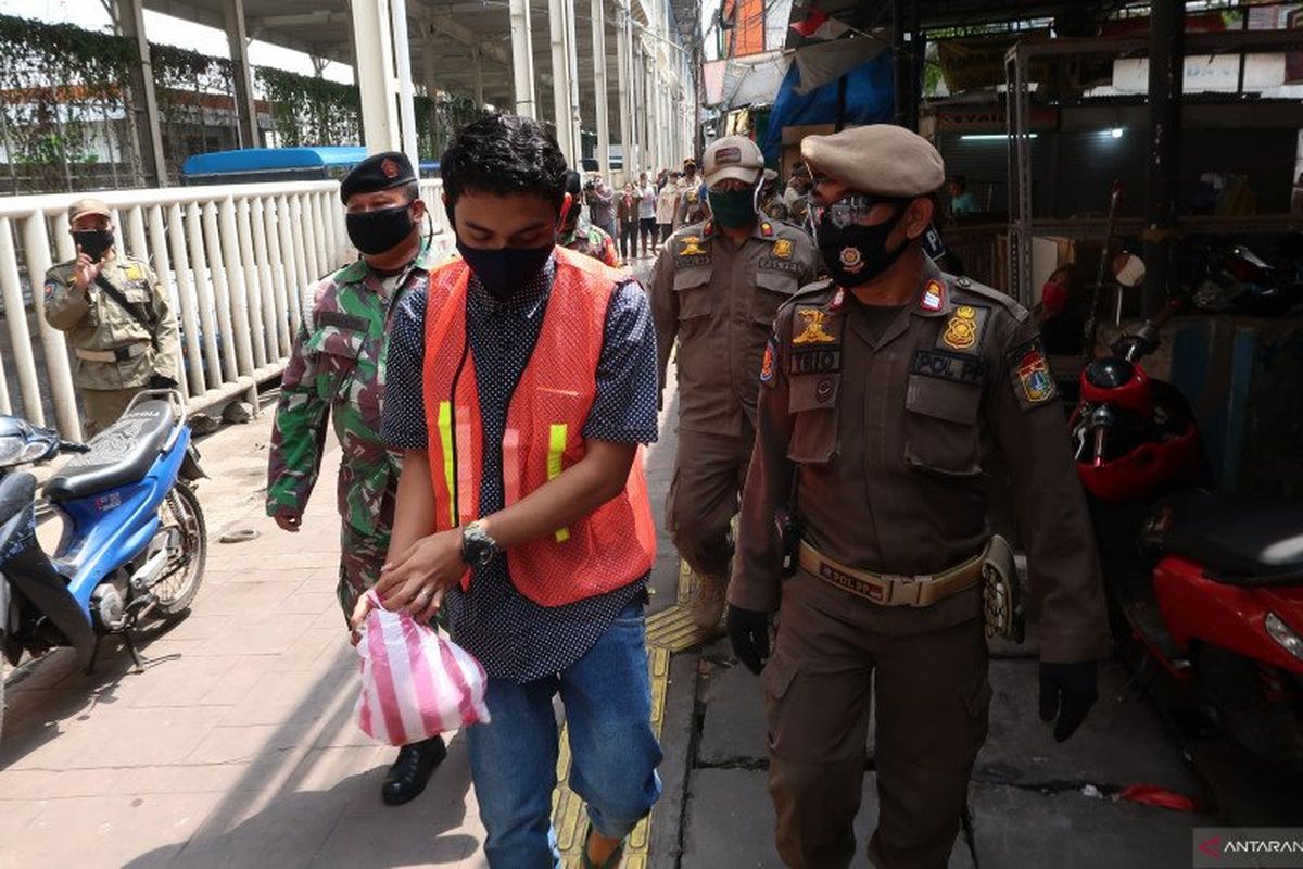 Pelanggar PSBB menerima sanksi memakai rompi oranye dan memungut sampah di kawasan Tanah Abang, Jakarta Pusat, Rabu (13/5/2020). (Sugiharto Purnama)
