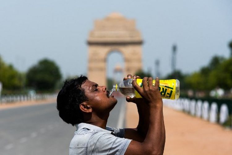 Seorang pekerja menghilangkan dahaganya dengan air botol istirahat dari membersihkan rumput pembohong dari taman dekat India di tengah suhu naik akibat gelombang panas di New Delhi pada 27 Mei 2020. 