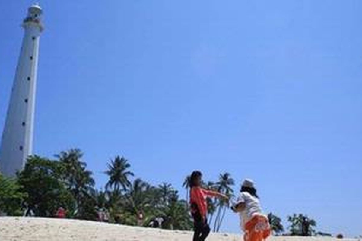 Wisatawan tengah berfoto dengan latar belakang mercusuar peninggalan Belanda di Pulau Lengkuas, Belitung