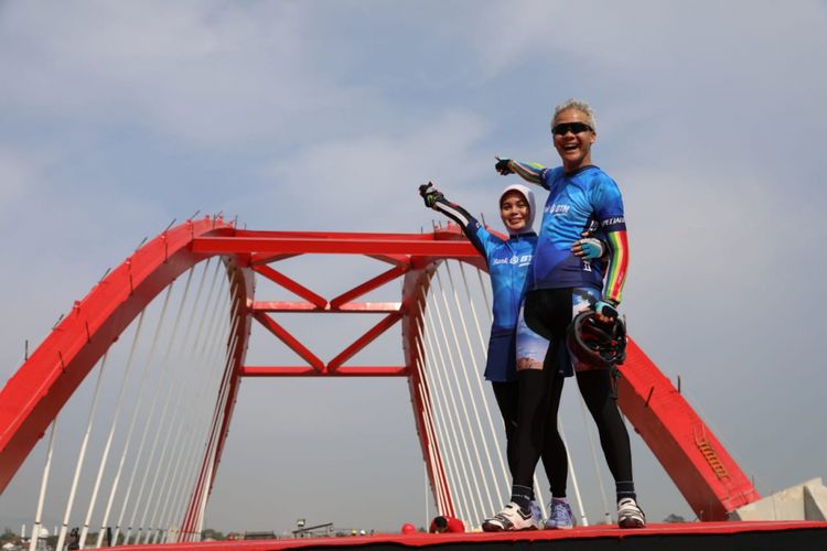 Gubernur Ganjar Pranowo dan istri Siti Atikoh berfoto dengan latar belakang jembatan merah putih Kalikuto yang menjadi ikon jalan tol Semarang-Batang seusai menyelesaikan BTN Tour de Borobudur XVIII 2018 etape I Semarang-Jembatan Kalikuto, Sabtu (3/11/2018).

 