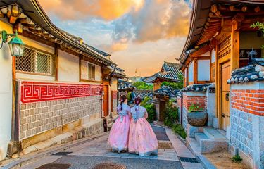 Ilustrasi Korea Selatan - Dua orang wisatawan sedang menggunakan hanbok dan berjalan-jalan di Bukchon Hanok Village, Korea Selatan.