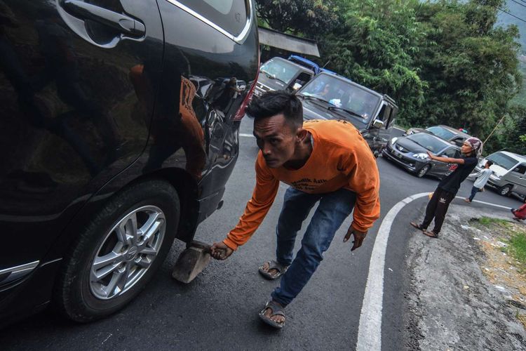 Seorang tukang ganjal mengganjal ban mobil pemudik yang tidak kuat melintas pada arus balik H+2 Lebaran di Tanjakan Gentong, Kabupaten Tasikmalaya, Jawa Barat, Jumat (7/6/2019).