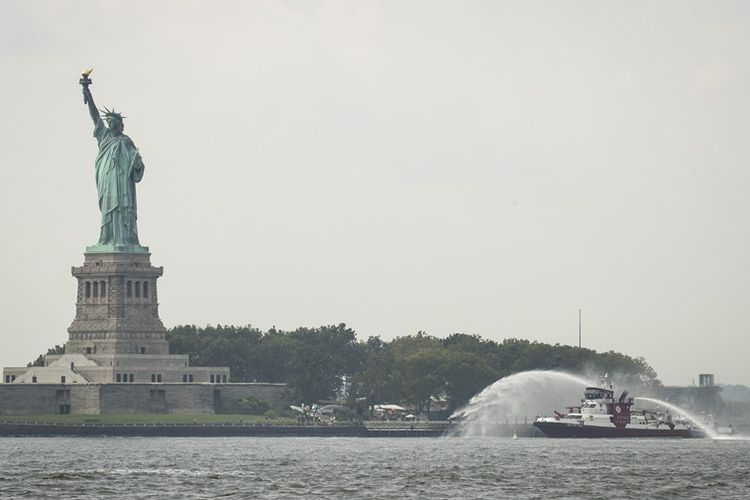 Kapal pemadam dari Departemen Pemadam Kebakaran New York menyemprotkan air ke lokasi kebakaran di dekat patung Liberty, Senin (27/8/2018).