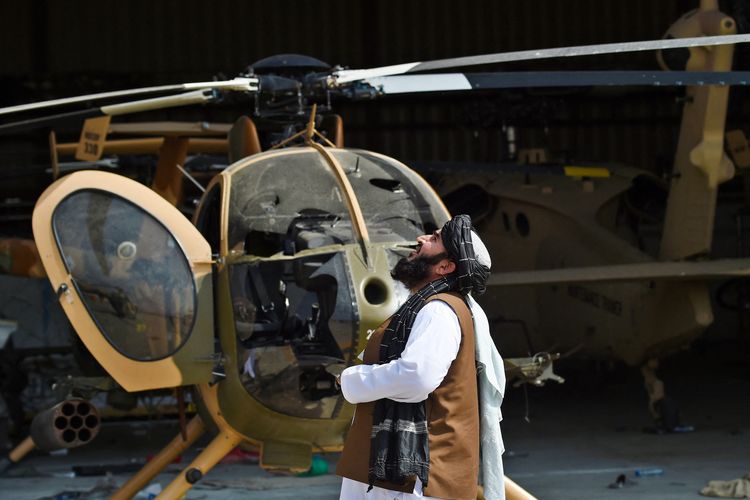 Seorang anggota Taliban memerhatikan helikopter rusak yang terparkir di bandara Kabul, pada 31 Agustus 2021.
