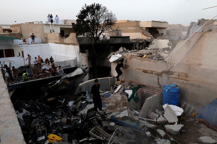 Orang-orang berdiri di atap rumah yang hancur menjadi puing-puing karena ditabrak pesawat Pakistan International Airlines (PIA) pada Jumat (22/5/2020). Kecelakaan terjadi di permukiman Karachi, salah satu kota terbesar di Pakistan.