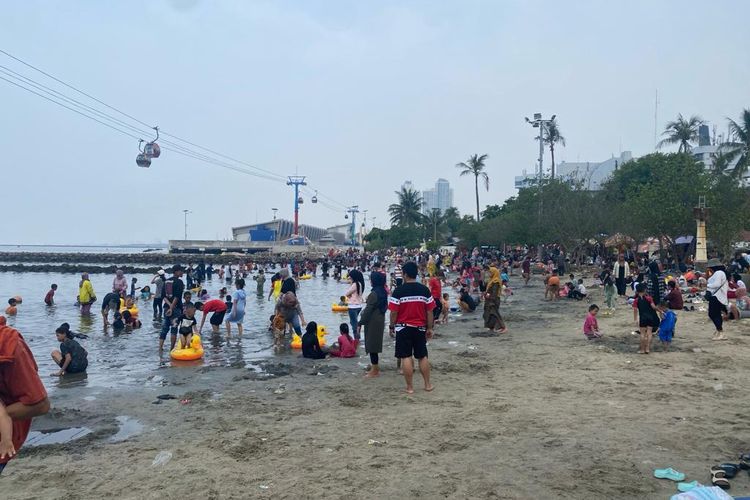 Sejumlah pengunjung Taman Impian Jaya Ancol tengah asyik bermain di bibir Pantai Indah, Senin (25/12/2023).