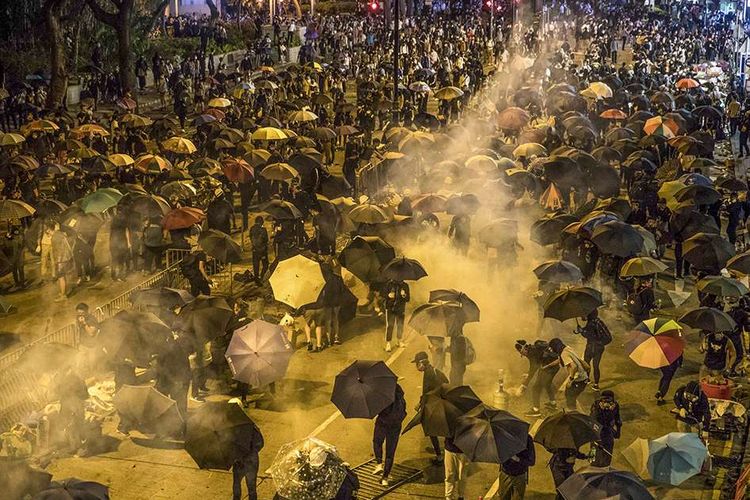 Para pengunjuk rasa berlindung ketika polisi menembakkan gas air mata ketika mereka berusaha menuju Universitas Politeknik Hong Kong di distrik Hung Hom, Hong Kong, Senin (18/11/2019). Kericuhan bermula dari aksi pendemo menduduki kampus selama beberapa hari hingga berujung aksi lempar dan bentrokan dengan polisi.
