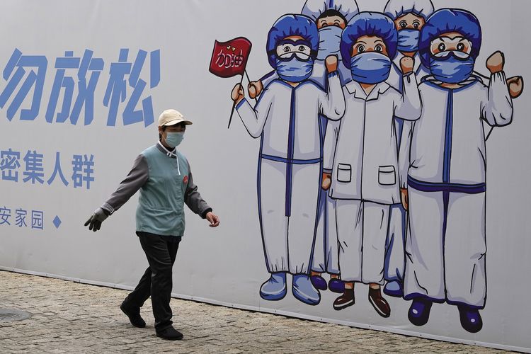 Seorang petugas kebersihan memakai masker berjalan di depan papan bergambar kartun tenaga kesehatan yang memerangi Covid-19 dengan kalimat Jangan Lengah, di Beijing, China, Kamis (14/10/2021).