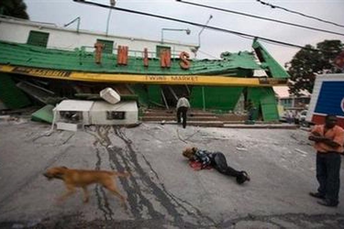 Seorang perempuan terlihat terbaring di tanah sementara yang lainnya berdiri di luar sebuah pasar yang ambruk akibat guncangan gempa di  Port-au-Prince, Haiti, Selasa (12/1/ 2010). 