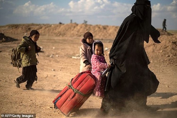 Seorang ibu berjalan sambil membawa tas koper dengan bayinya di atas, dan diikuti dua anaknya ketika meninggalkan Baghouz, kota di Suriah yang menjadi benteng terakhir ISIS.