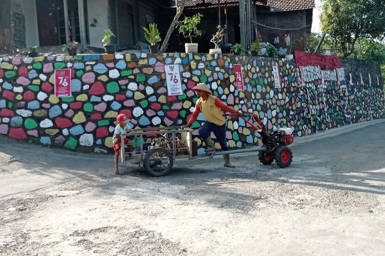 Petani di Kampung Meri melintasi dinding batu yang dicat warn awarni pemuda desa yang menginginkan perubahan desa mereka di masa pandemi covid 19.