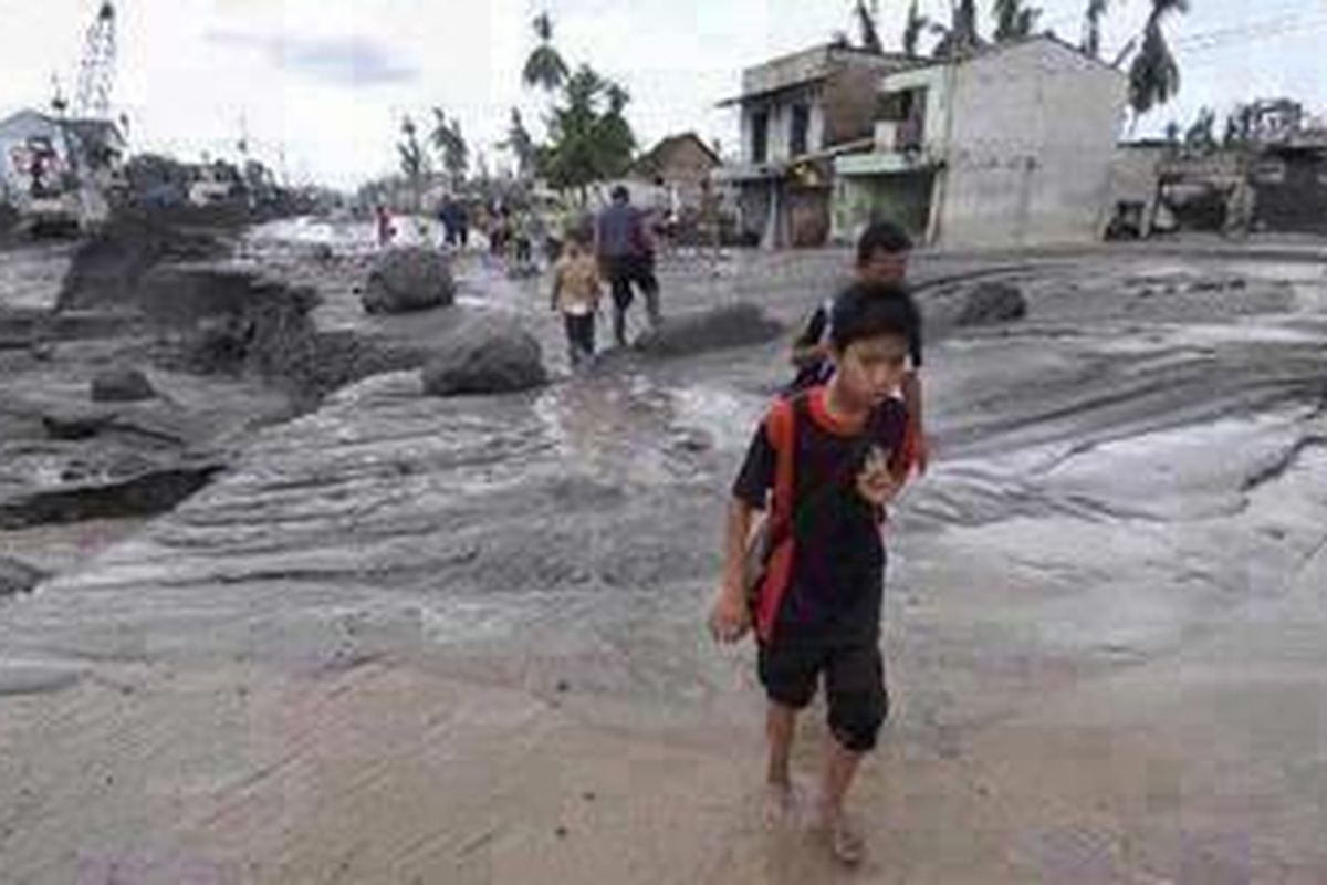 Pelajar melewati endapan material Gunung Merapi yang terbawa banjir lahar dingin di Jalan Yogyakarta-Magelang, Desa Jumoyo, Salam, Magelang, Jawa Tengah, Jumat (4/2/2011). Selain mengakibatkan jalur utama Yogyakarta-Magelang terputus, banjir lahar dingin juga mengakibatkan sejumlah tiang beton yang baru saja dipasang untuk memperkuat pondasi jalan menjadi miring. 