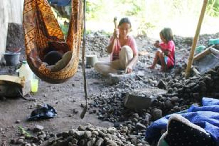 Tummi (37) memecahkan batu di Kolong Jembatan, Argasunya, Harjamukti, Kota Cirebon, Senin (22/12/2014). Ia memecahkan batu sambil mengasuh anaknya yang tertidur di ayunan.