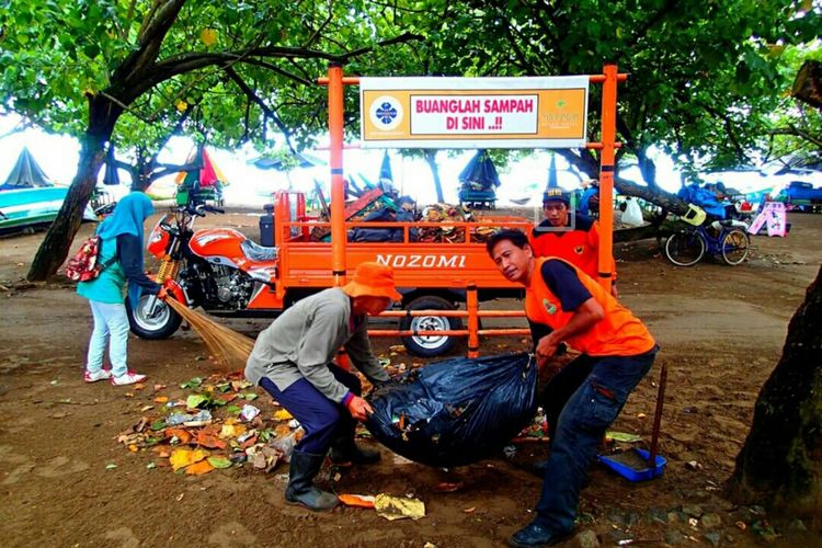 Rosyid (kanan) dan rekannya sedang menaikan sampah ke kendaraan pengangkut sampah di Pantai Barat, Pangandaran.