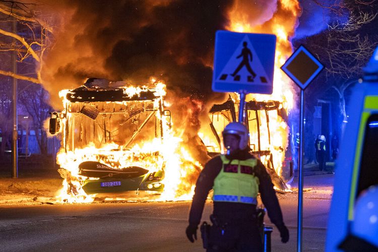 Polisi anti huru hara menyaksikan sebuah bus kota terbakar di sebuah jalan di Malmo, Swedia, Sabtu, 16 April 2022. 