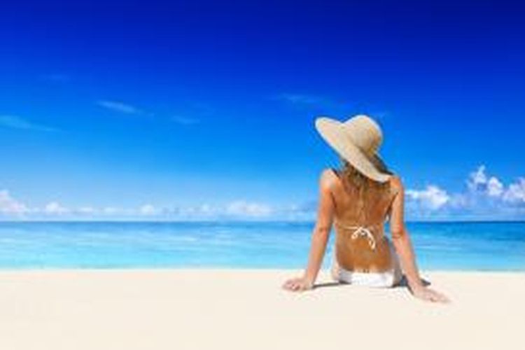 ILUSTRASI - Seorang turis perempuan berjemur di pantai.
