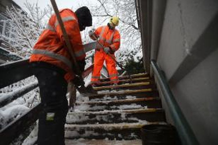 Para pekerja membersihkan serpihan es dari tangga yang menuju ke stasiun kereta bawah tanah di Brooklyn, New York, AS, akibat badai salju terbesar yang pernah menghantam negeri itu.