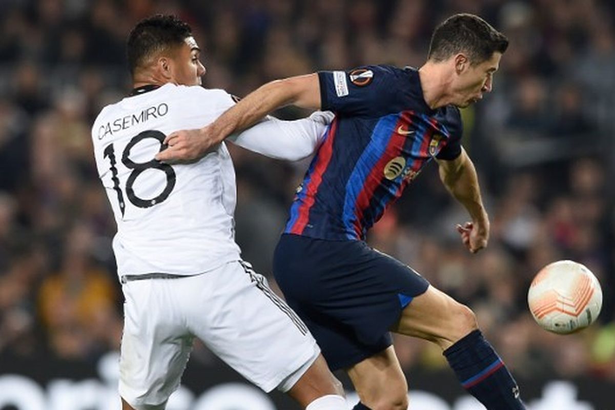 Gelandang Man United, Casemiro, ketika berduel dengan striker Barcelona, Robert Lewandowski, dalam leg pertama playoff knock-out Liga Europa 2022-2023 di Stadion Camp Nou pada 16 Februari 2023. Artikel ini berisi jadwal Liga Europa yang menghadirkan laga Man United vs Barcelona. (Photo by Josep LAGO / AFP)