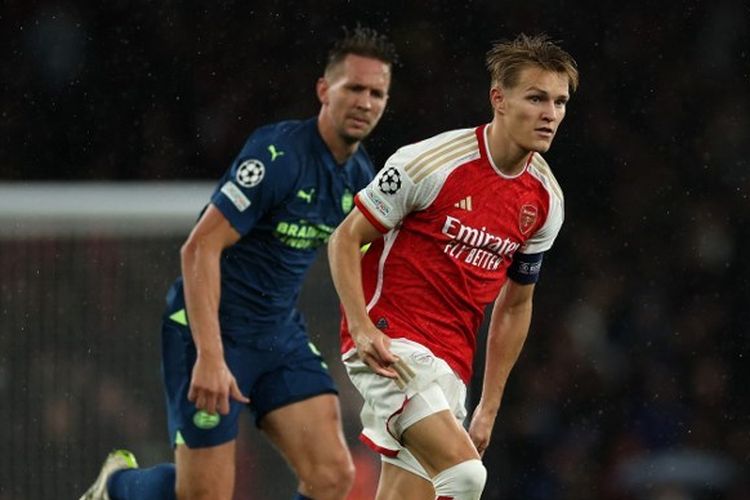 Gelandang sekaligus kapten Arsenal, Martin Odegaard (kanan), dibayangi pemain PSV Eindhoven dalam laga matchday pertama Grup B Liga Champions 2023-2024 yang digelar di Stadion Emirates, London, pada Rabu (20/9/2023) malam waktu setempat. (Foto oleh Adrian DENNIS / AFP)