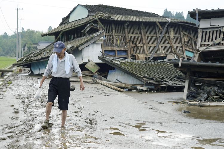 Seorang pria berjalan di jalanan yang terendam lumpur usai banjir besar di Desa Kuma, Prefektur Kumamoto, Jepang, pada Minggu (5/7/2020). Hujan deras di Kumamoto memicu banjir besar dan tanah longsor, yang membuat puluhan orang terjebak di rumah dan bangunan-bangunan lainnya.