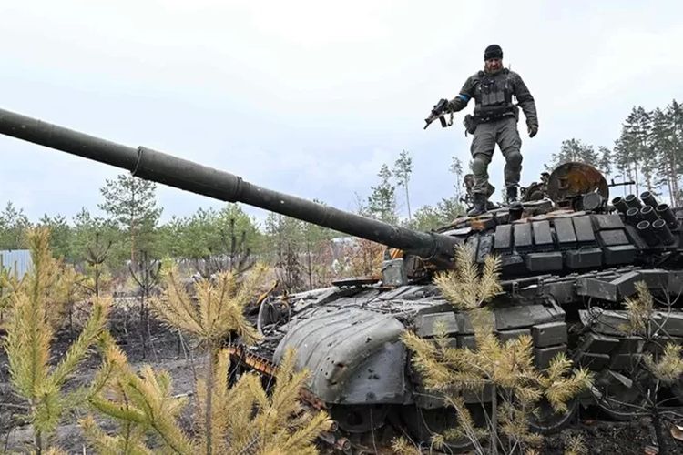 Seorang tentara menghancurkan tank Rusia di dekat ibu kota Kyiv.

