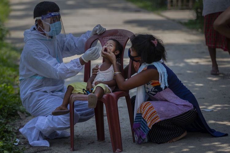 An Indian health worker in protective suit takes the swab of a child to test for COVID-19 in Burha Mayong village, Morigaon district of Assam, India, Saturday, May 22, 2021. (AP Photo/Anupam Nath)