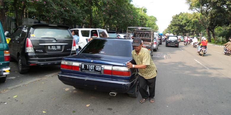 Seorang tukang parkir di Jalan Medan Merdeka Selatan, Jakarta, tengah mendorong mobil agar mobil lain bisa keluar, Kamis (31/7/2014). UP Perparkiran DKI Jakarta memastikan aktivitas mereka adalah ilegal.