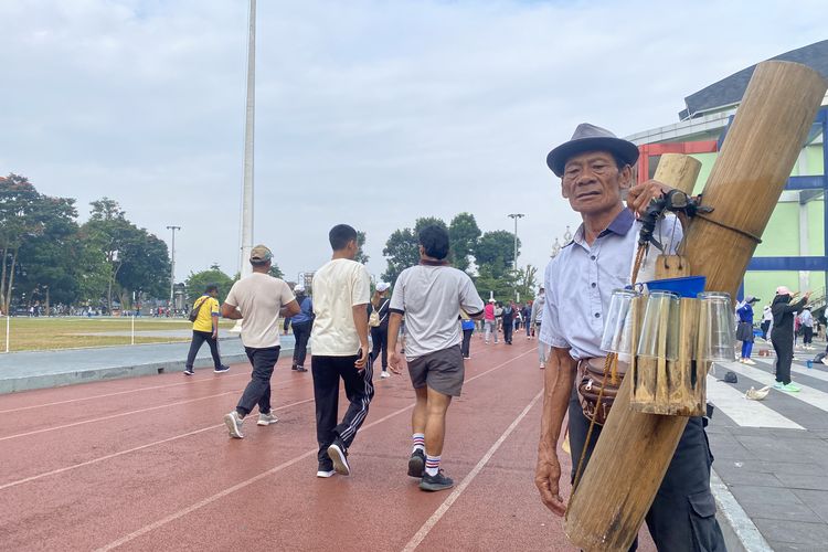 Asep tengah berdiri dengan memilkul bambu yang berisi air lahang untuk dijual di area Lapang Merdeka Kota Sukabumi.