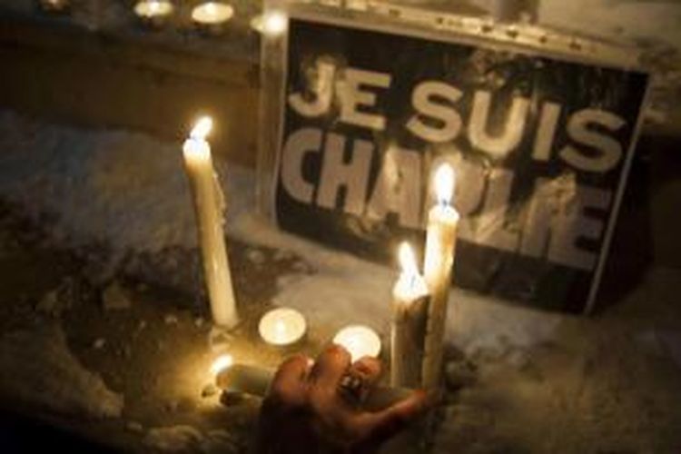 Seorang wanita Albania menyalakan lilin di dekat tulisan dalam bahasa Perancis 'Saya Charlie', saat berkumpul di Pristina, untuk mendukung kebebasan pers menyusul serangan bersenjata ke kantor satir Charlie Hebdo, Rabu (7/1/2015).