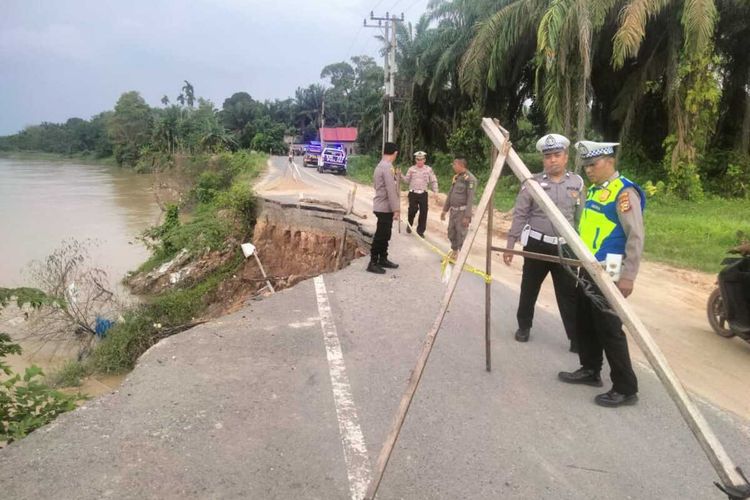Petugas kepolisian memasang rambu peringatan di ruas jalan penghubung antar kecamatan yang ambles, di Kabupaten Indragiri Hulu, Riau, Selasa (18/4/2023).